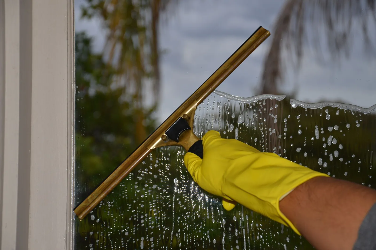 Fensterabzieher und gelber Handschuh auf einer eingeschäumten Glasscheibe