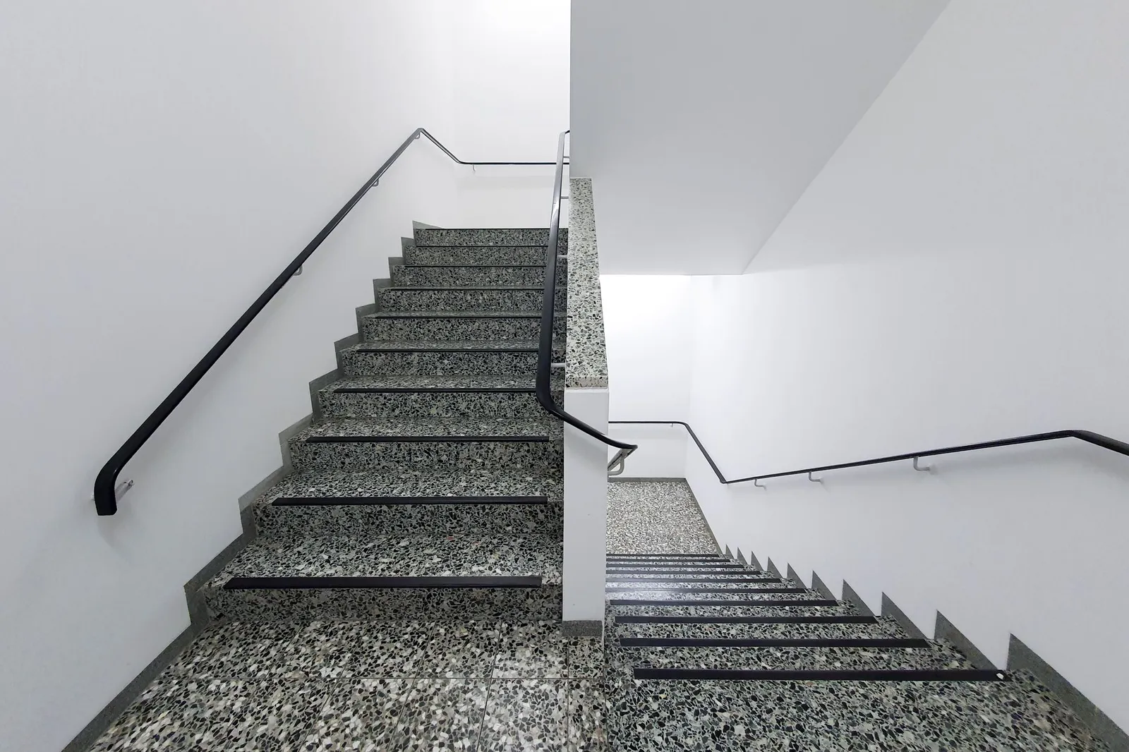 Helles Treppenhaus mit Steinstufen und schwarzem Handlauf
